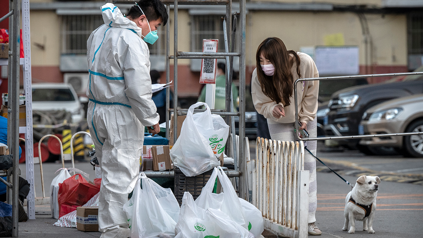 A woman looks at items arrived as a guard wears protective clothing at a community that is locked down due to COVID-19 on April 28, 2022 in Beijing, China. 