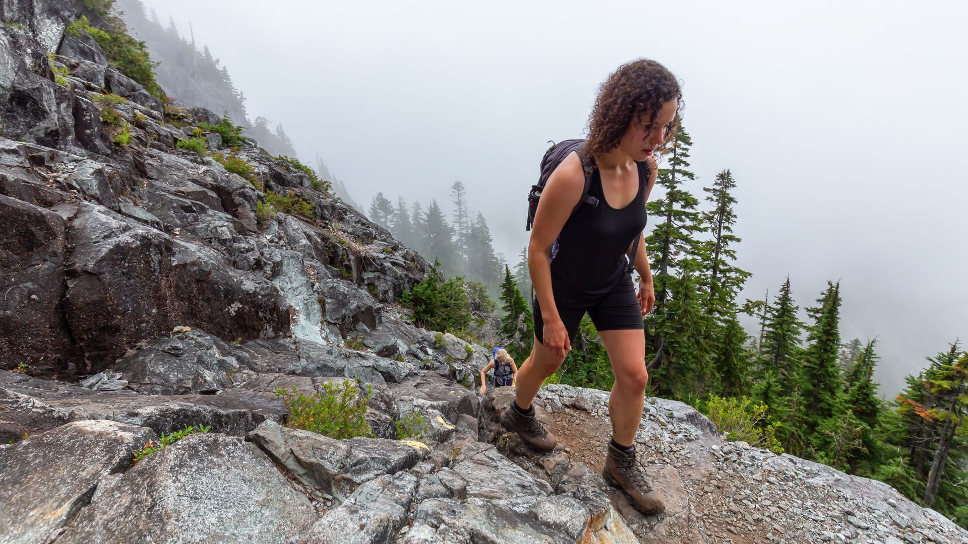 Woman hiking rocky mountain trail using walking sticks for hiking stability