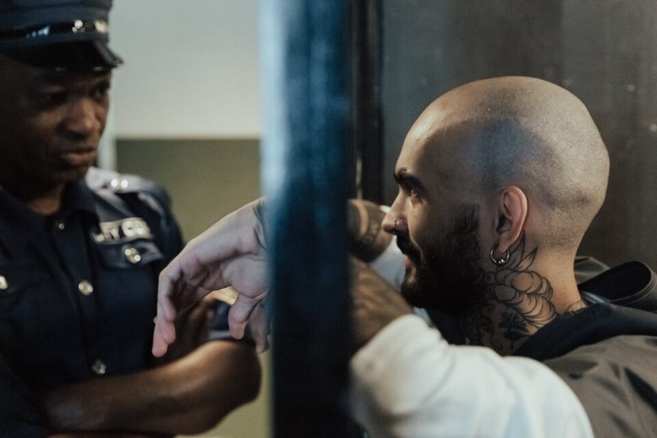 Photo by Ron Lach : https://www.pexels.com/photo/bald-man-with-tattoo-in-jail-near-a-policeman-10475164/